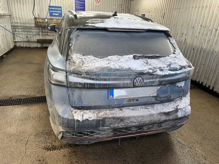 Bil i en tvätthall, bakifrån sedd, täckt med smuts och is efter vinterkörning.