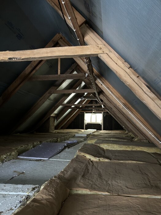 Loft med synlige trebjelker og isolasjonsmatter, mulig prosjekt for heving av tak eller utgraving for bedre takhøyde i huset fra 1909.