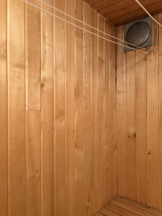 Bastuvägg med trävåder och en rund ventil i hörnet, del av diskussion om byte av bastuaggregat och ventilationslösning i källarbastu.