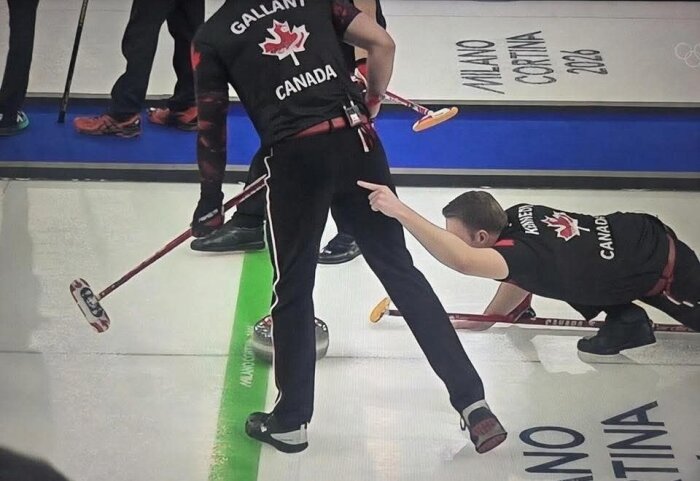 Curlingspelare från Kanadas lag i aktion på isen under en match. En spelare pekar medan en annan sveper framför stenen.