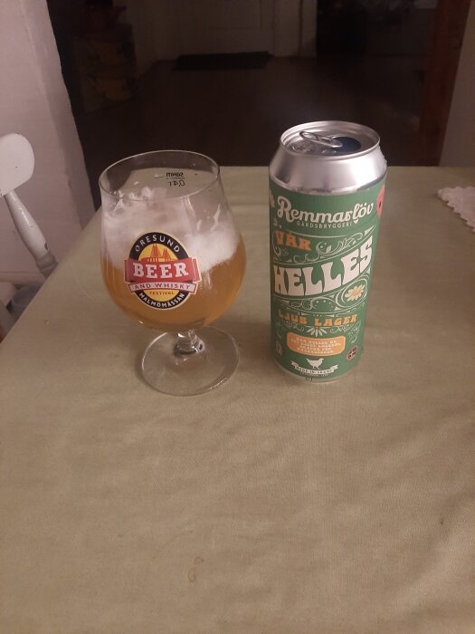 Ett ölglas med öl bredvid en burk Remmarlöv Vår Helles lager på ett bord.