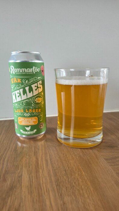 En burk med Remmarlöv Vår Helles öl bredvid ett glas fyllt med ljus lageröl på ett bord.
