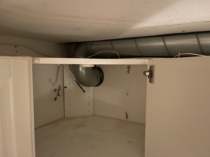 Öppen köksskåp med synligt ventilationsrör utan isolering, elektriska kablar hänger inuti.