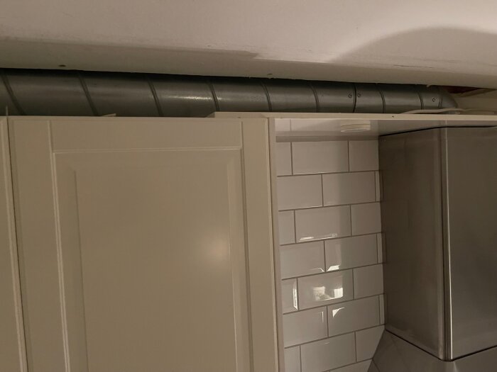 Köksfläktsrör över vit kökskåpa och kakel, utan isolering.