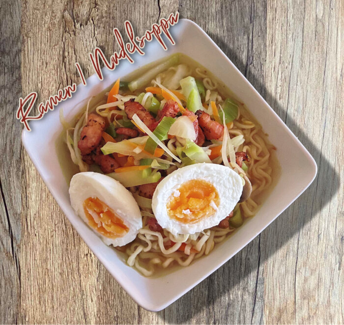 Skål med ramen nudelsoppa, innehållande grönsaker, stekt fläsk och kokt ägg, med texten "Ramen i Nudelsoppa".
