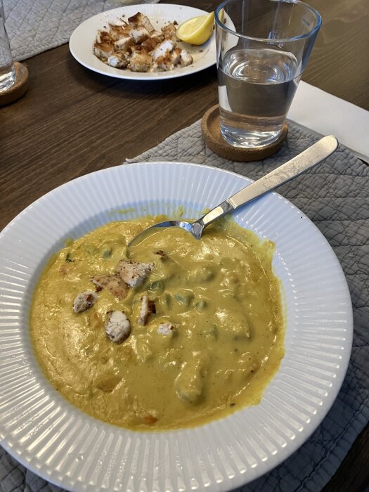 Slätmixad indisk linssoppa med kyckling och paprika serverad i en vit tallrik. Bredvid finns ett glas vatten och en tallrik med citronskiva och grillad kyckling.