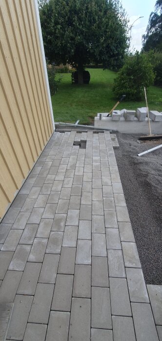 Nybelagd stenläggning intill en ljus träfasad, med en gjuten betongmur och platta för postlåda synlig i bakgrunden.
