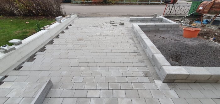 Stenlagd gång och betongmur med osorterade stenar. Gjuten platta längst bort ska bära en ny postlåda.
