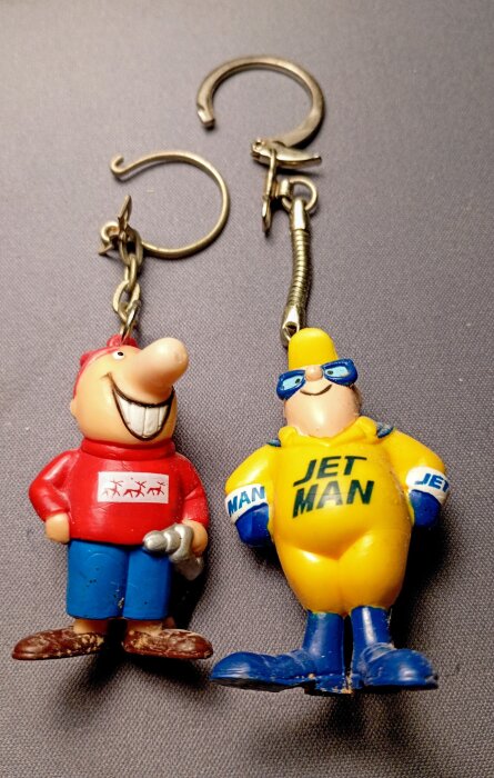 Två nyckelringar med figurer av gamla bensinstationsmärken, en i röd tröja och en "JET MAN" i gult.