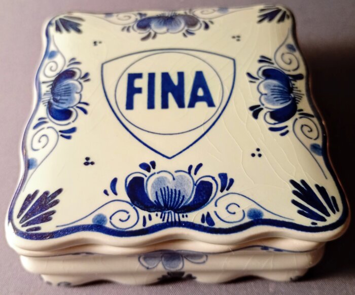 Blå-vitt keramikföremål med texten "FINA" och blomdesign, relaterat till nostalgiska bensinstationsmärken.