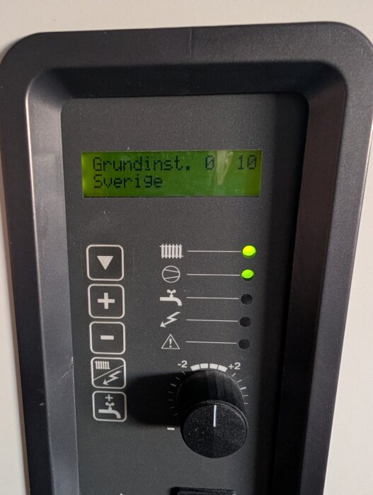 Användarpanel på värmepump med displayen som visar "Grundinst. Sverige". Justeringsratt och lysdioder är i fokus.