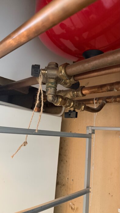 Vattenrör och ventiler i en värmepumpinstallation, med en röd expansionskärl i bakgrunden. Endast en synlig avstängningsventil på röret.