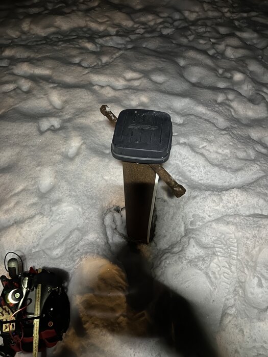 Brunnslock i snöigt landskap, med ett metallföremål placerat över. En verktygslåda syns bredvid.