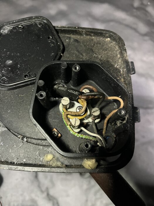 Öppen elbox med exponerade kablar och anslutningar, del av ett vattenpumpsystem. Smutsig yta, tecken på ålder och slitage.
