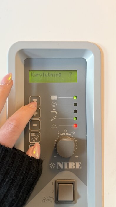En person justerar inställningen på en NIBE-värmepump, displayen visar "Kurvlutning 7".