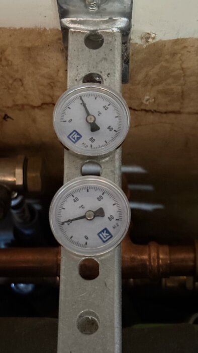 Två termometrar monterade på en metallplatta visar temperaturer i ett VVS-system.
