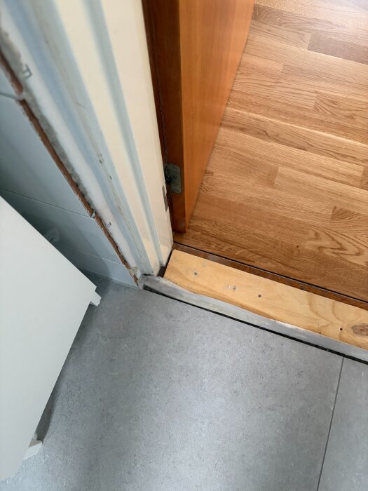 Bild av dörrkarm och tröskel i ett renoverat badrum med tätskikt synligt vid golvet.