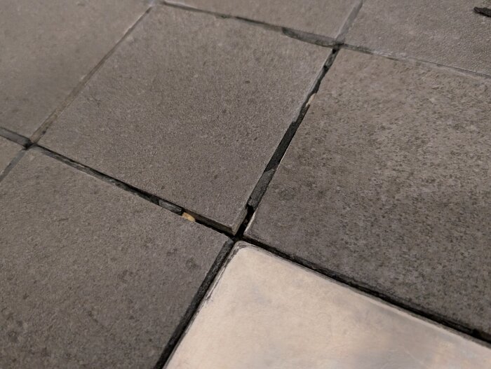 Spruckna fogar och lösa kakelplattor på duschgolv, indikerar potentiell skada i badrum.