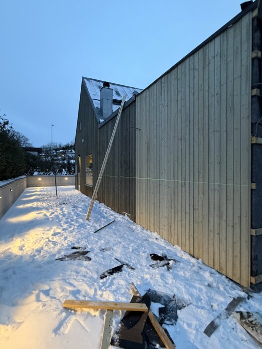 Person spikar panel på ett hus i snötäckt område, järnvitriolbehandlad träpanel. Laserlinje och snö syns i förgrunden.