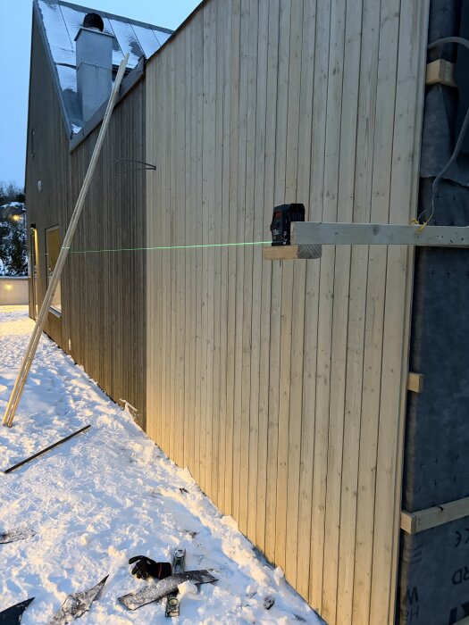 Järnvitriolbehandlad träpanel på husfasad i vintertid, med laserverktyg för mätning och byggutrustning i snön.