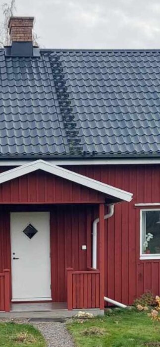 Rött hus med farstukvist och plåttak, skorsten synlig. Utmaning med halt papptak för sotare, diskussion om lösningar och offert för steg och brygga.