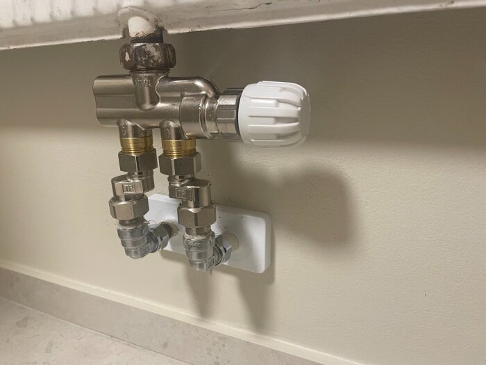 Närbild på anslutningen av rör till ett element, med justeringsventiler och metallkopplingar i en tvättstuga eller badrum.