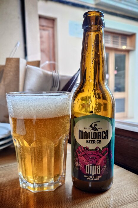 Flaska och glas med öl, etikett "Mallorca Beer Co" och "Double India Pale Ale", står på bord med oskarp bakgrund.