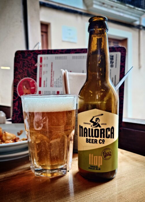 Flaska och glas med Mallorca Beer Co IPA på ett bord med menyer i bakgrunden.
