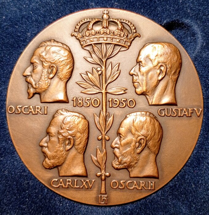 Bronserad medalj med porträtt av svenska kungar och årtalen 1850-1950, detaljerade sniderier och en krona överst.
