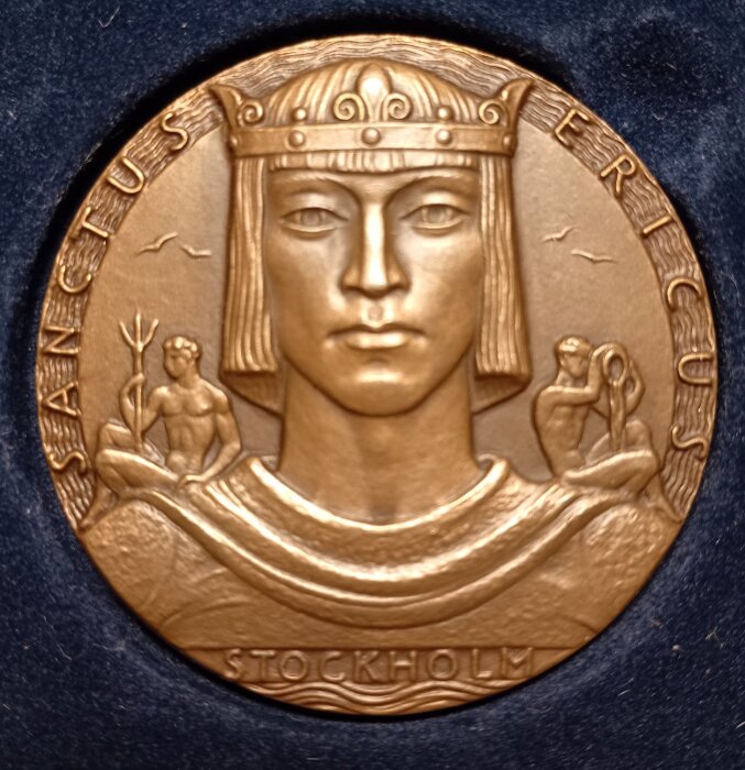 Medaljong med huvudet av en person med krona, inskriptioner ”Sanctus Ericus” och ”Stockholm” omgiven av detaljerade figurer och mönster.