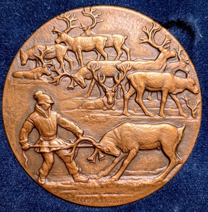 Medalj av Leo Holmgren med detaljerad avbildning av renar och en människa i traditionell klädsel, graverad i en scen av samisk kultur.