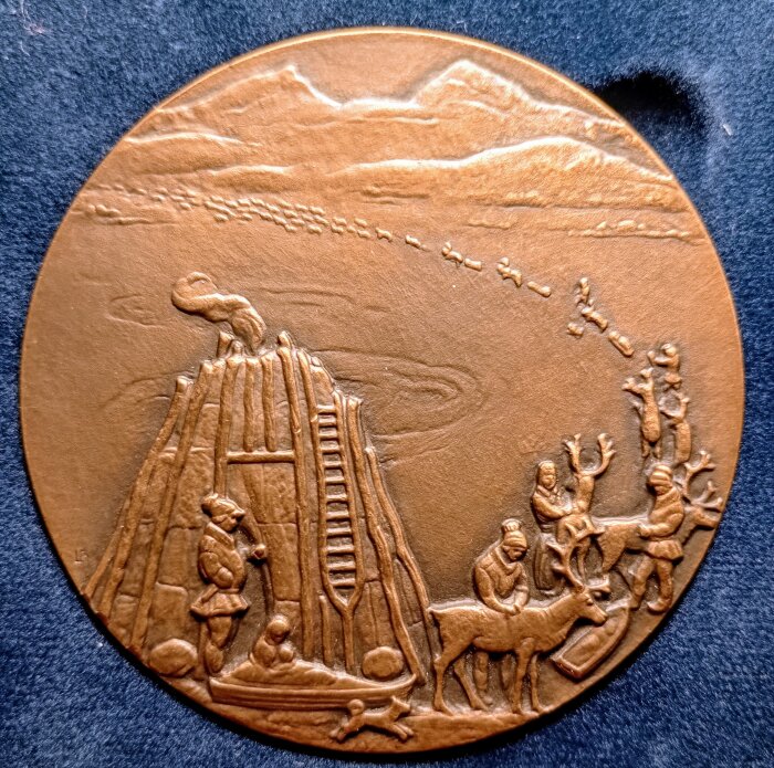 Medalj med detaljerat motiv av människor och renar vid en kåta, med en stege och fjäll i bakgrunden, skapad av Leo Holmgren.