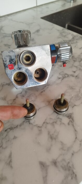Gammal blandare av fabrikatet Mora med backventiler och metallsätena lossade, placerade på en marmorerad yta.