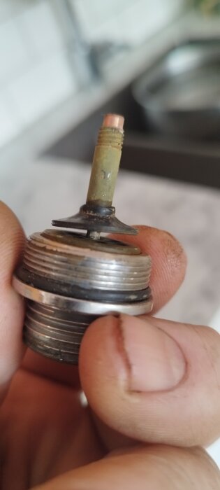 En man håller en del av en äldre Mora-blandare med gummitätning och metallgängor, relevant för diskussion om byte av backventiler.