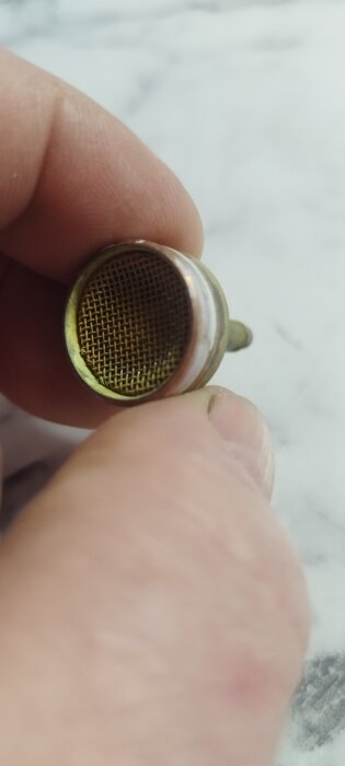 Närbild av en metallisk backventil med galler där gummiflärpar från en Mora-blandare från 80-talet har tagits bort.