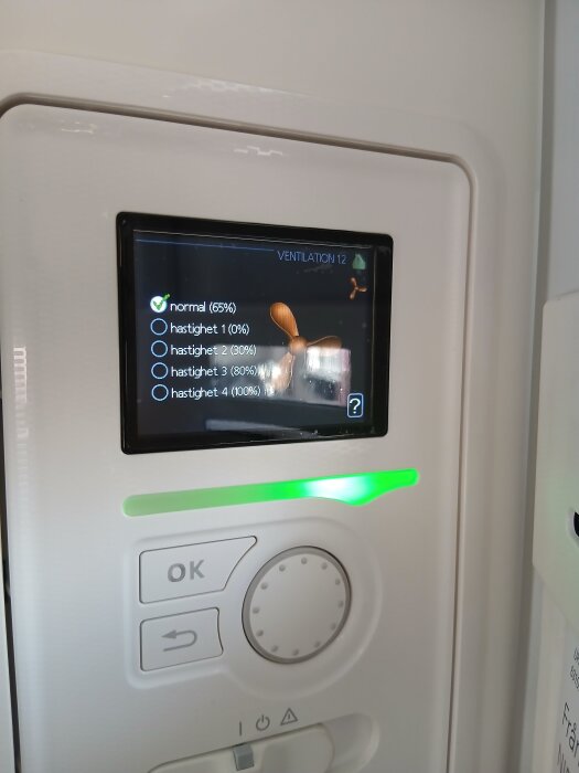 Kontrollpanel för ventilationssystem med en digital display som visar olika hastighetsinställningar, en ratt och knappar för att justera inställningarna.