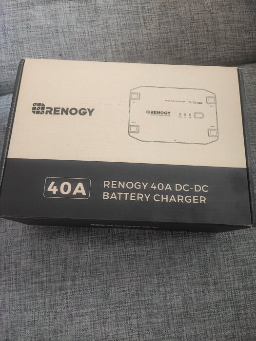 Förpackning av en Renogy 40A DC-DC batteriladdare på en grå soffa.
