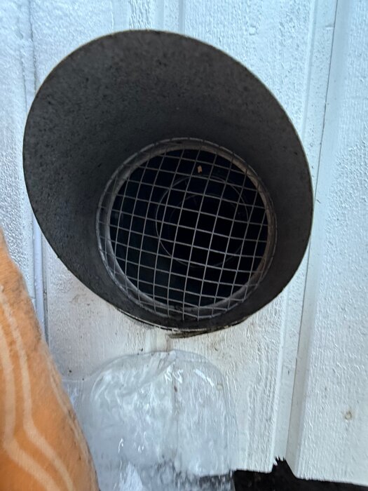 Ventilationsrör på en vägg med isbildning nedanför, troligtvis från en radonsug, vilket orsakar skador på fasaden och marken.