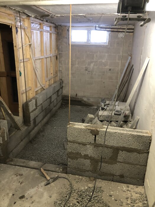 Källarrenovering med pågående murarbete, innervägg byggs med 120mm breda stenar. Verktyg och material synliga i bilden.