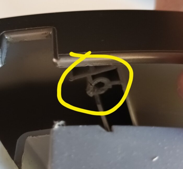 Skadat skruvfäste, markerat i gult, nära gångjärn på en apparatlucka, där fästet har knäckts och behöver repareras eller bytas ut.