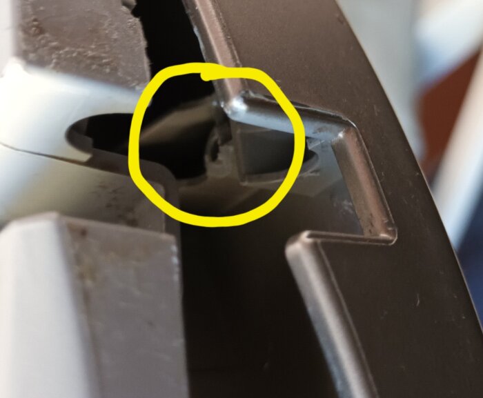Närbild på en trasig skruvfäste vid en lucka med ett gult cirkulärt märke som visar skadan.