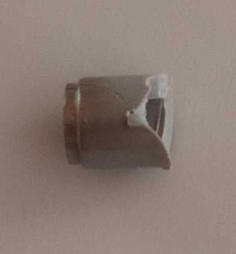 Brutet skruvfäste från en lucka, delvis trasigt vid kanten.