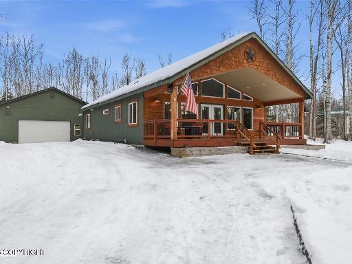 Hus i vinterlandskap med snö, veranda med amerikansk flagga, omgiven av träd.