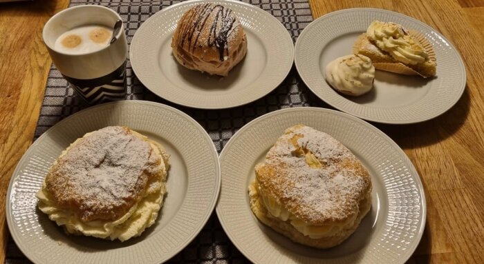 Tallrikar med Wienersemlor, en Nutellasemla, en biskvi och en bit kladdkaka, serverade med en kopp kaffe.