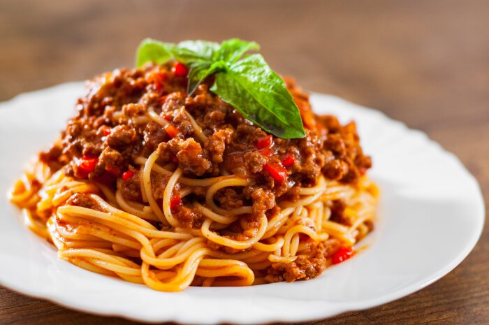 Spagetti med köttfärssås toppad med färska basilikablad, serverad på en vit tallrik.