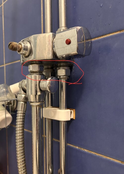 Duschblandare med två kopplingar och en röd knapp monterad på blått kakel, med synliga vattenrör och beslag.
