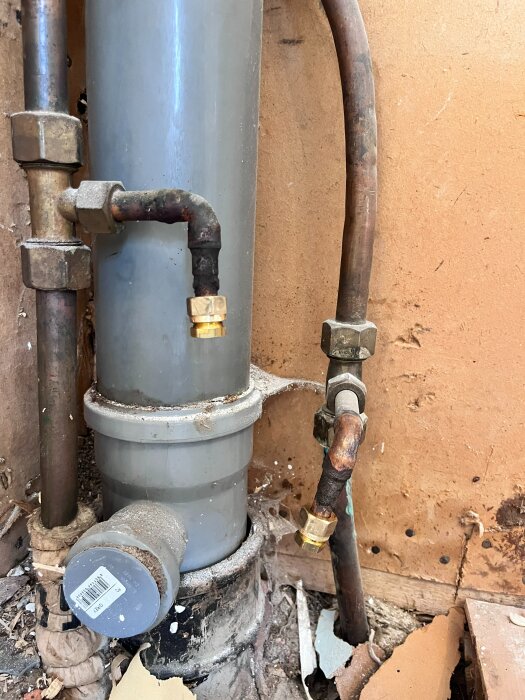 Två kapade grenrör med pluggade ändar i ett gammalt VVS-system, rör av olika material i en äldre villa.