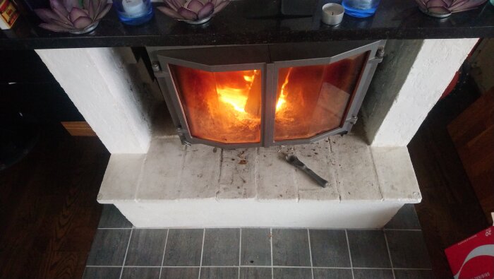Braskamin med glasdörrar i eld, en skiftnyckel liggande framför, synlig skillnad i lutning.