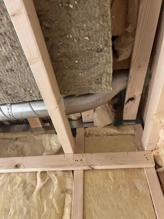 Ventilationskanal av aluminiumslang och spirorör monterad i ett innertak med träreglar och isolering.