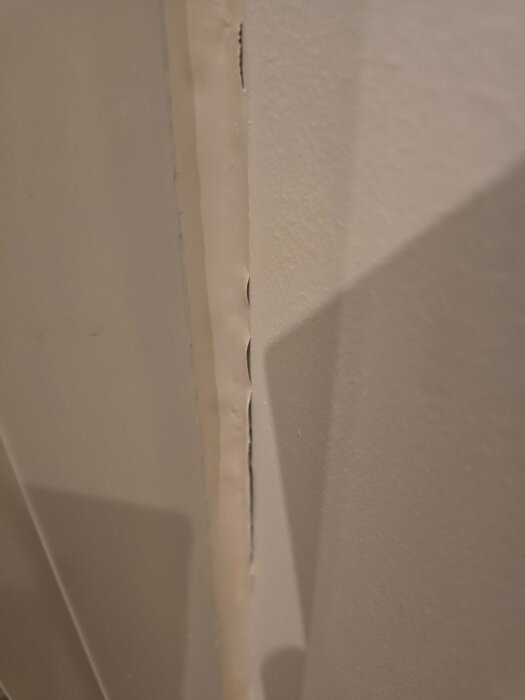 Fog runt balkongdörr som släpper från väggen, med synliga sprickor i silikonet.